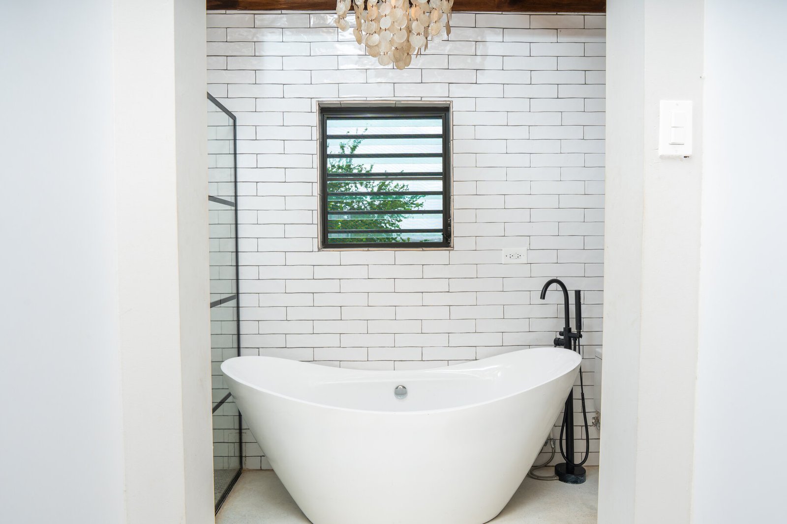 Freestanding tub beneath a shell chandelier and window with tree view