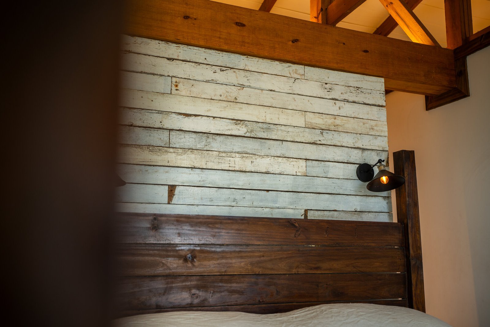 Bedroom headboard detail with reclaimed wood accent wall and sconce light