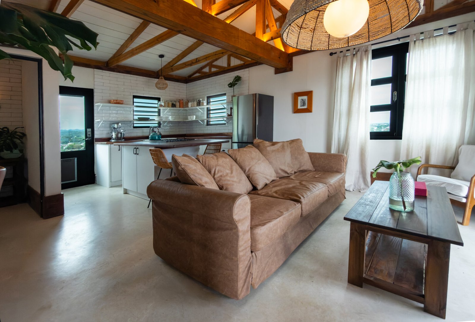 Open-concept living room with leather sofa, wood beams, and rattan pendant light